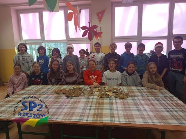 Uczniowie klasy 6 stoją za stołem, na którym leżą na talerzykach ozdobione pierniczki.