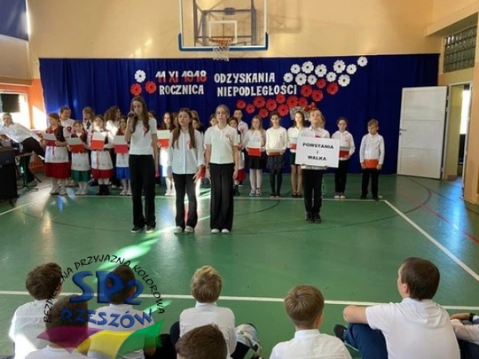 Uczniowie na sali gimnastycznej recytują wiersze z okazji święta niepodległości.