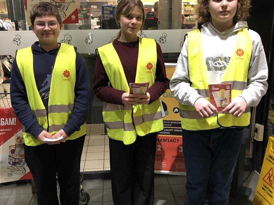 Uczniowie klas 8 w kamizelkach odblaskowych, rozdający ulotki akcji Caritas "Tak, Pomagam"