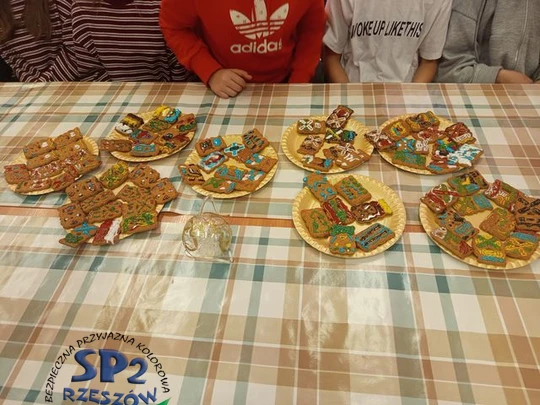 Na papierowych złotych talerzykach leżą pierniczki ozdobione kolorowymi pisakami.