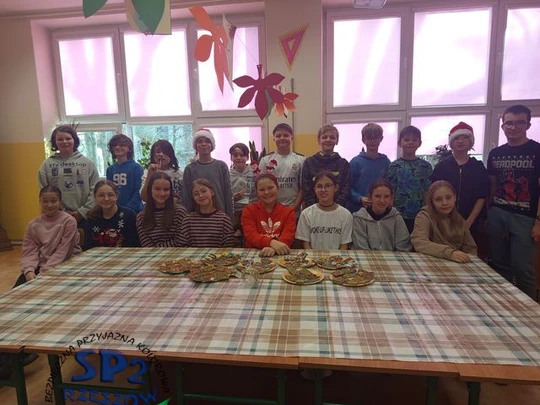 Uczniowie klasy 6 stoją za stołem, na którym leżą na talerzykach ozdobione pierniczki.
