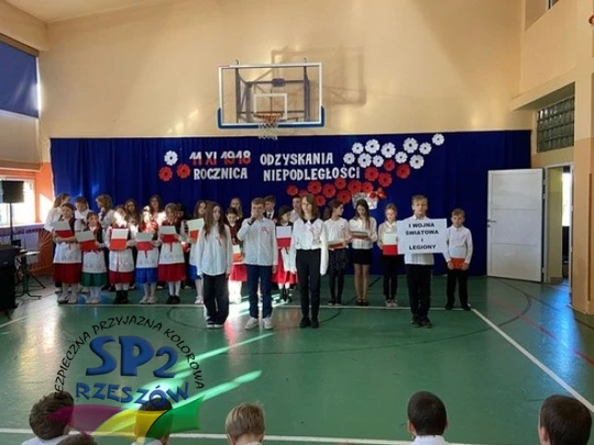 Dzieci w sali gimnastycznej śpiewają razem, uśmiechając się.