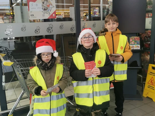 Uczniowie klasy 2b w kamizelkach odblaskowych, rozdający ulotki akcji Caritas "Tak, Pomagam"