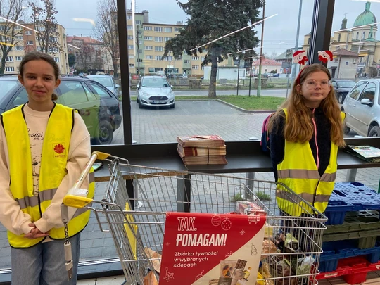 Uczennice w kamizelkach odblaskowych, przy wózku z ofiarowanymi produktami w akcji Caritas "Tak, Pomagam"