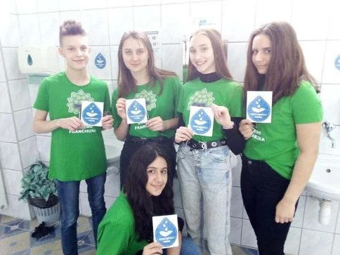 Uczennice przedstawiają naklejki, które będą umieszczać nad kranami.